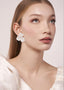 Woman wearing white floral earrings against a plain background