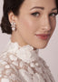 Close-up of a woman wearing pearl and crystal bridal earrings with a neutral background