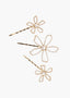 Set of three gold flower-shaped hair pins with pearl centers on a white background